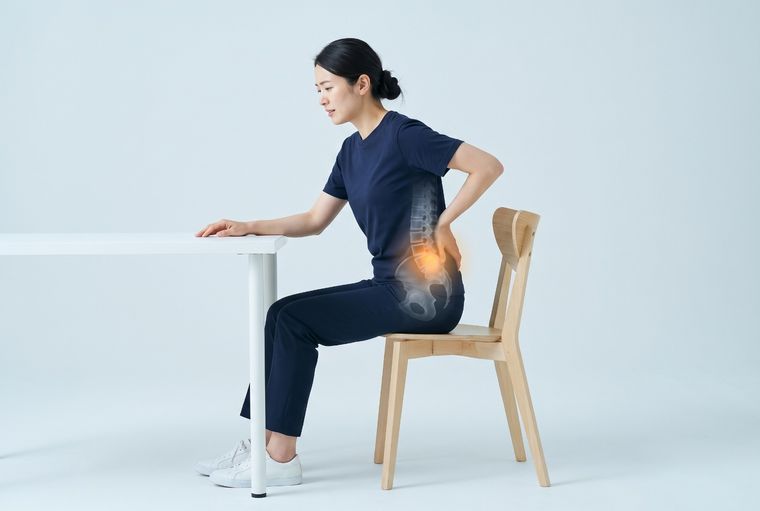 Self-check: sitting at a desk, leaning forward with a hand on the lower back, with one of the lower discs glowing.