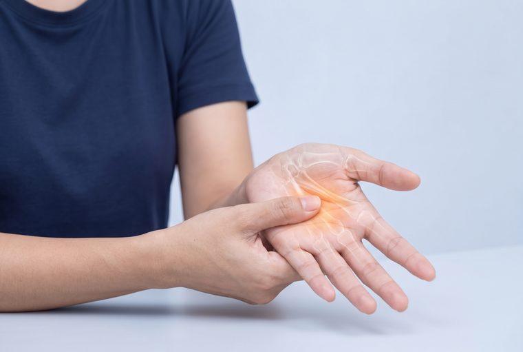 Pressing the thumb into the palm at the base of a finger to feel for a tender lump.